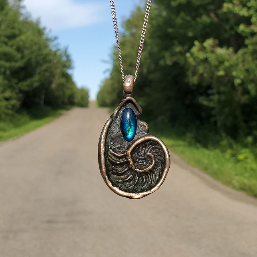 A shell-shaped flat pendant made out of bronze, with an abalone cabochon glued inside of it.